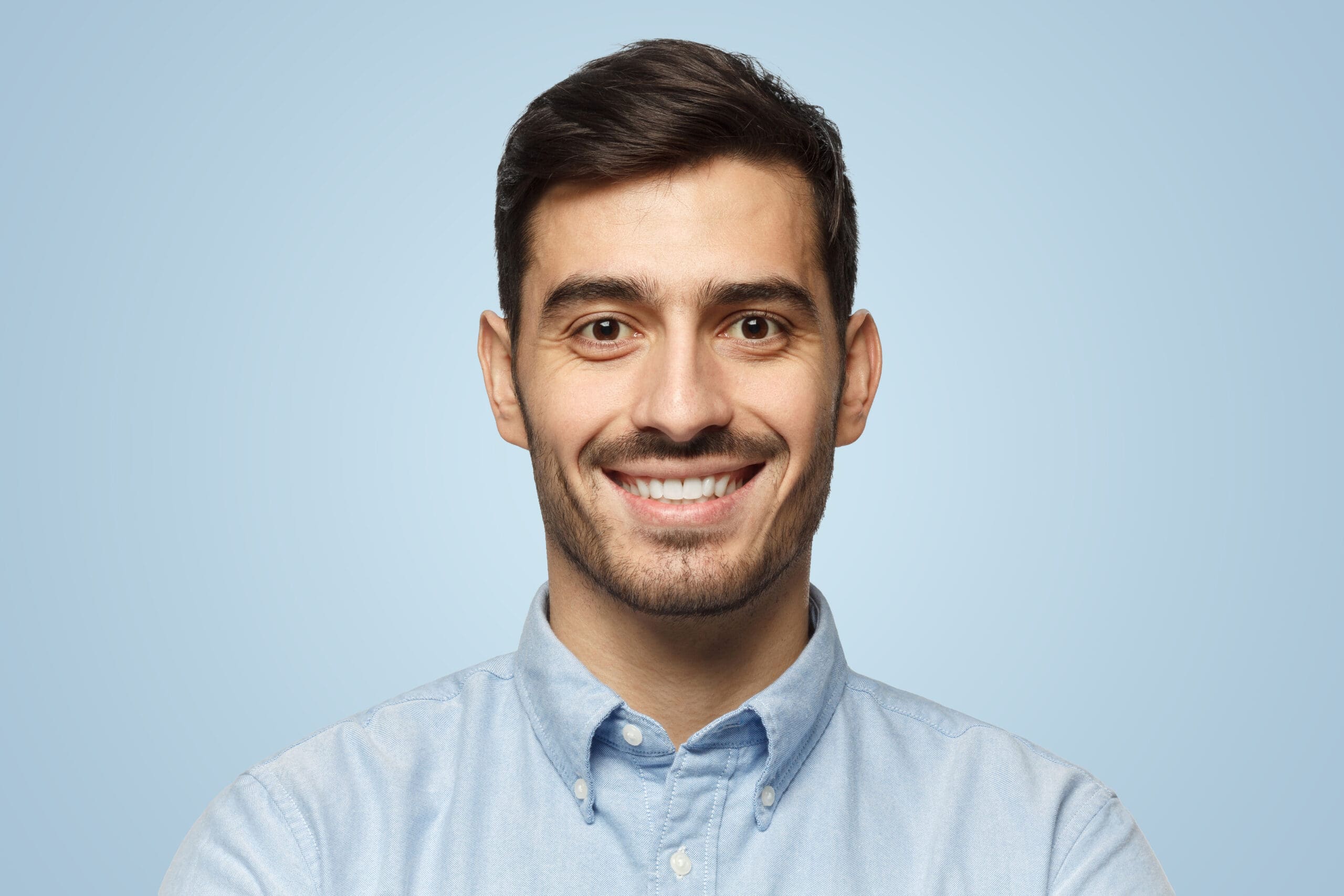Closeup headshot of businessman standing against blue background, smiling with satisfaction and confidence